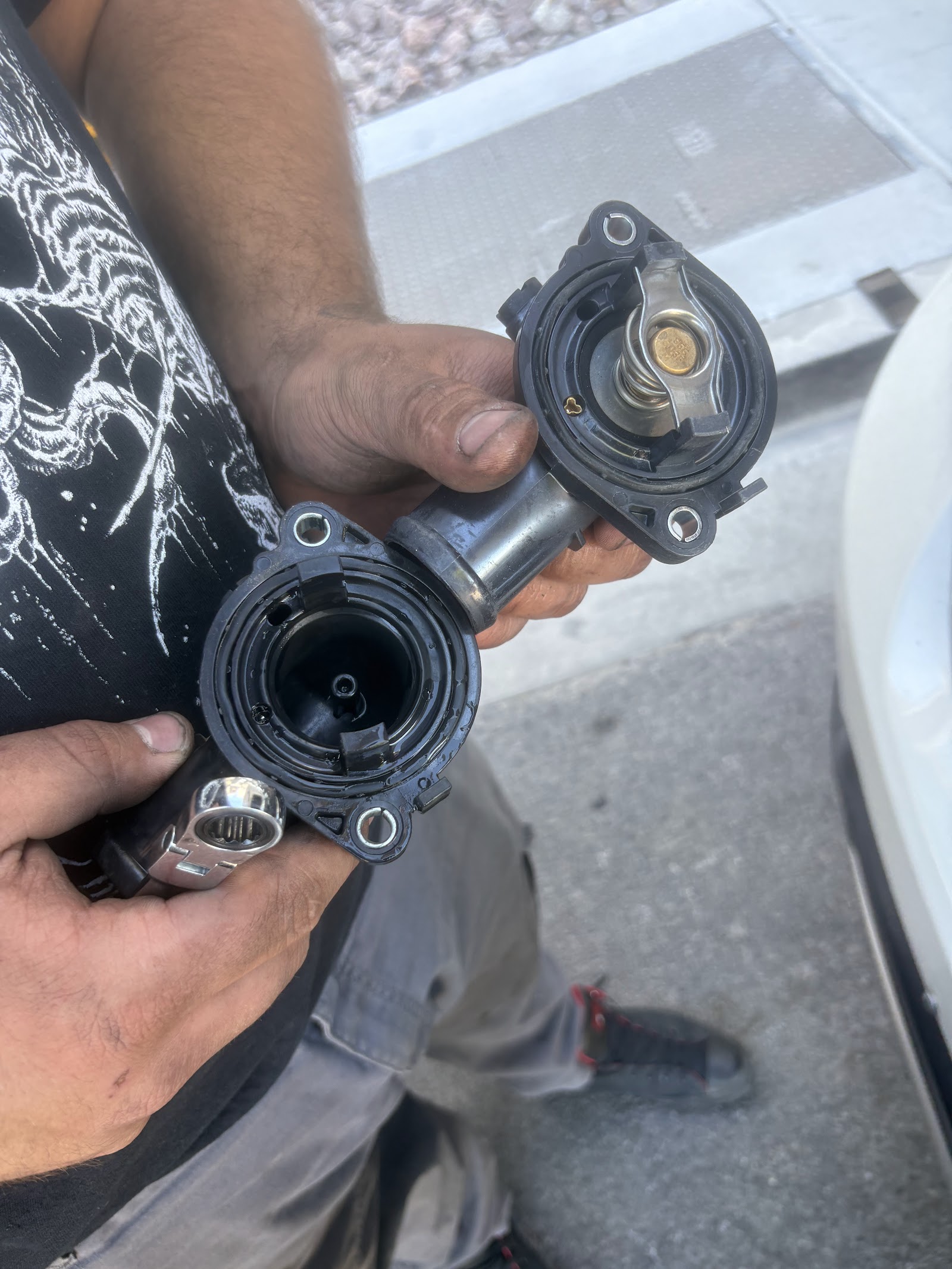 Mechanic holding disassembled thermostat housing and coolant components