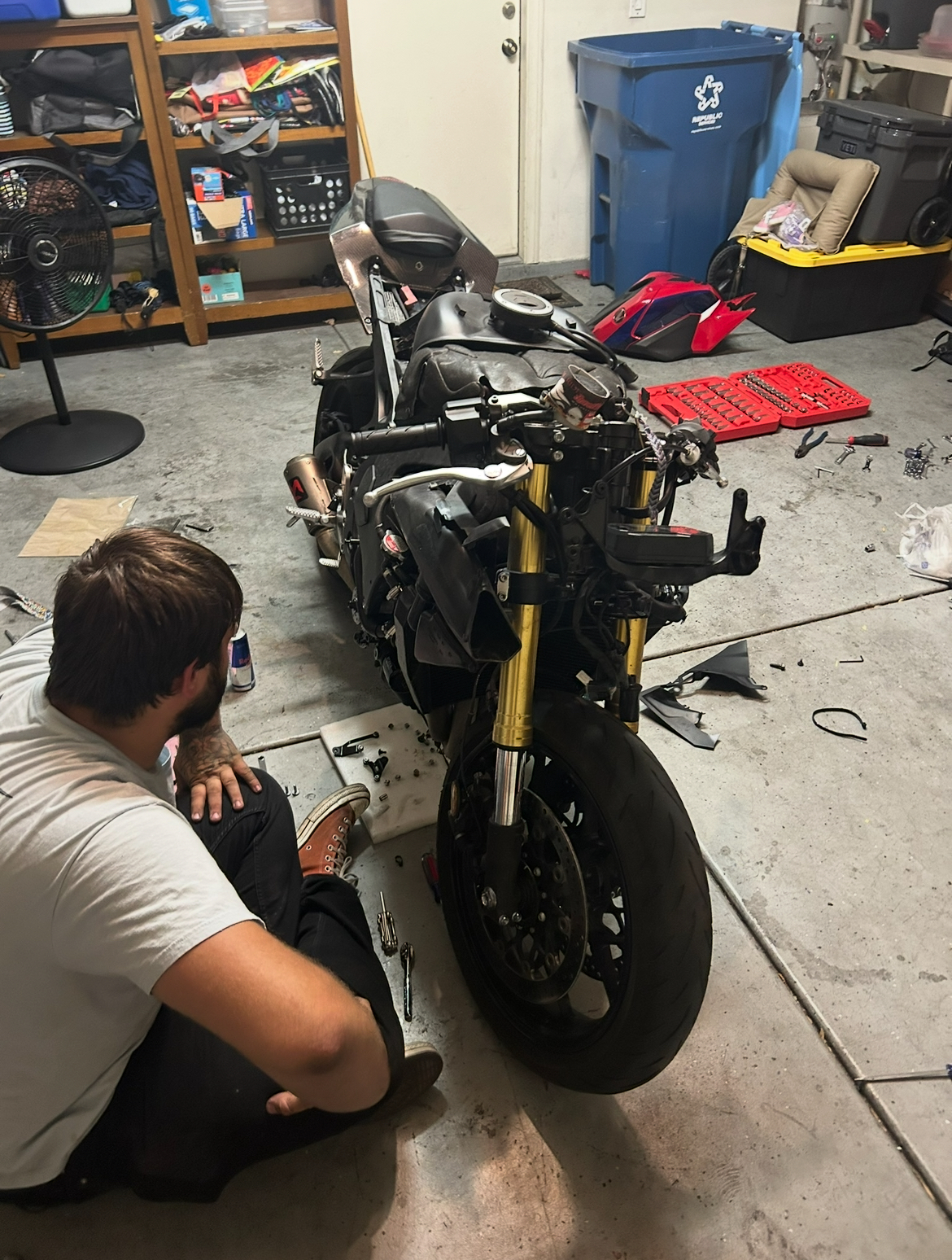 Technician working on a stripped sportbike motorcycle in a garage