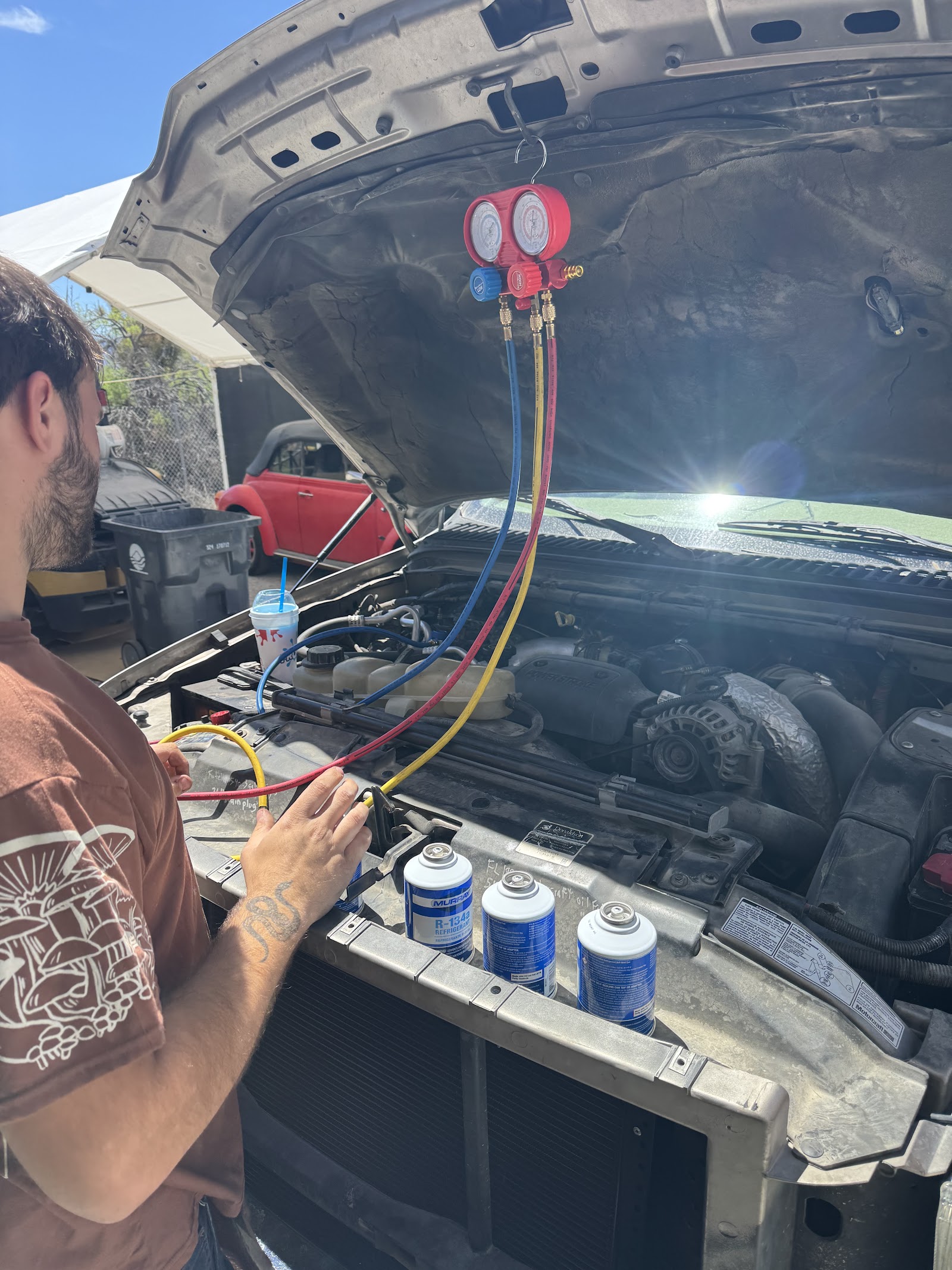 Mechanic recharging a vehicle A/C system with R-134a refrigerant and gauge manifold